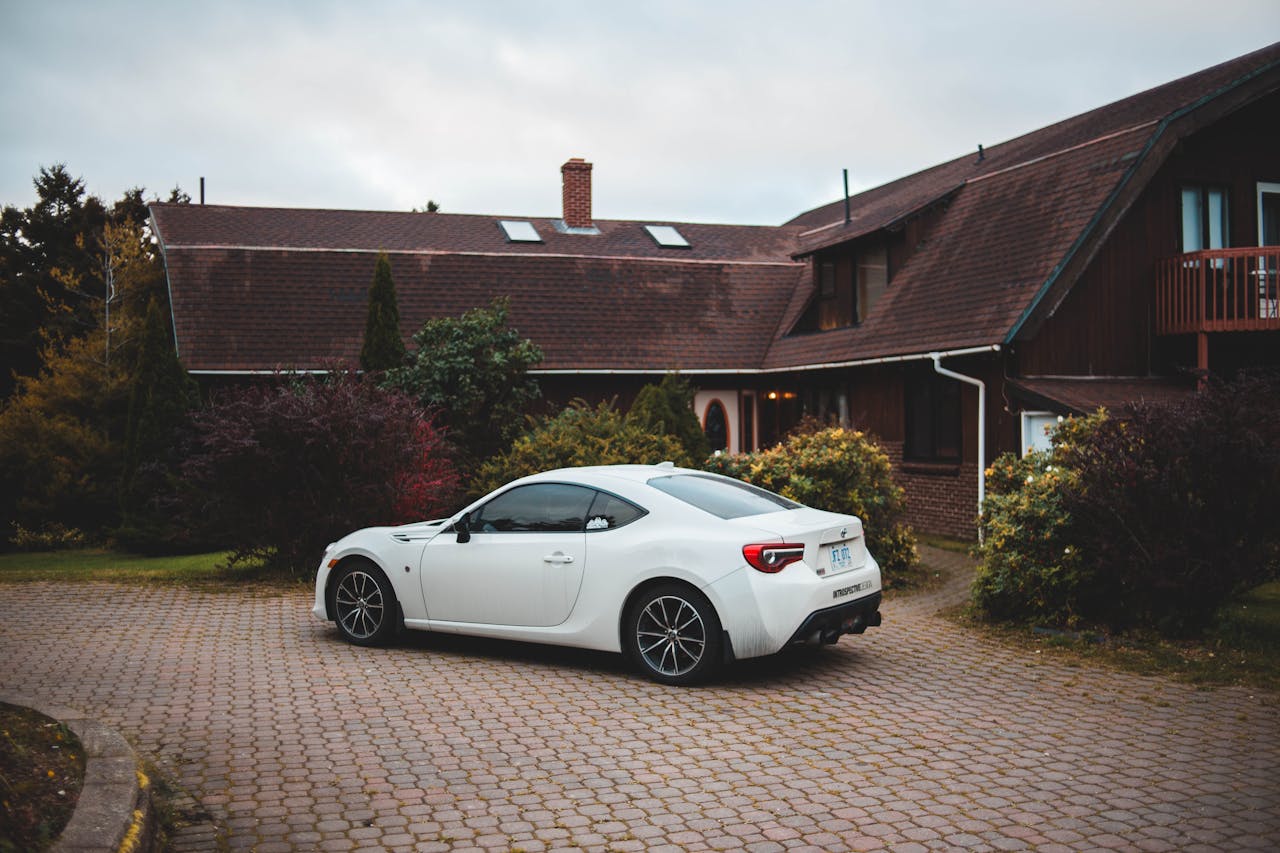 A sleek white sports car parked in front of a charming rustic house with well-kept gardens.
